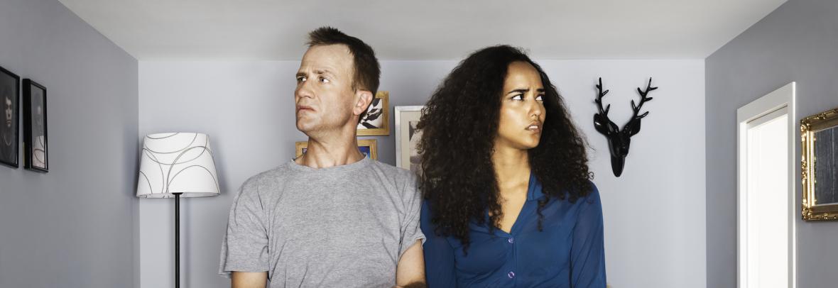 A confused couple sit in a tiny couch inside a tiny home