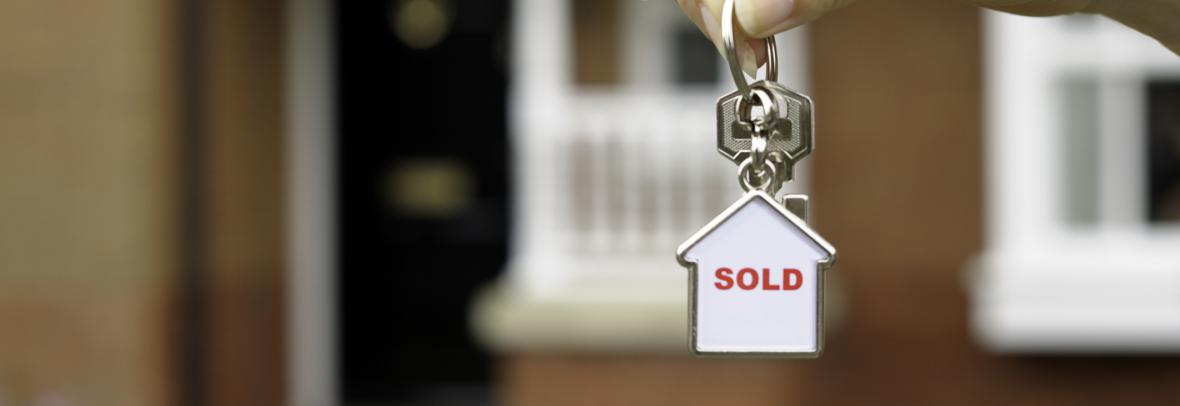 Hand in front of a house holding keychain with "sold" inside small house