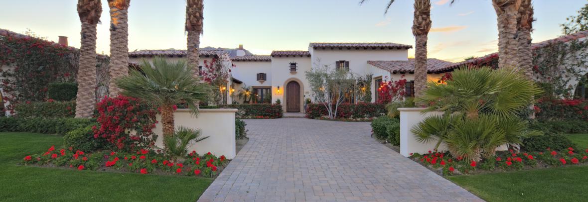Large luxury home with landscaped entryway bordered by palm trees