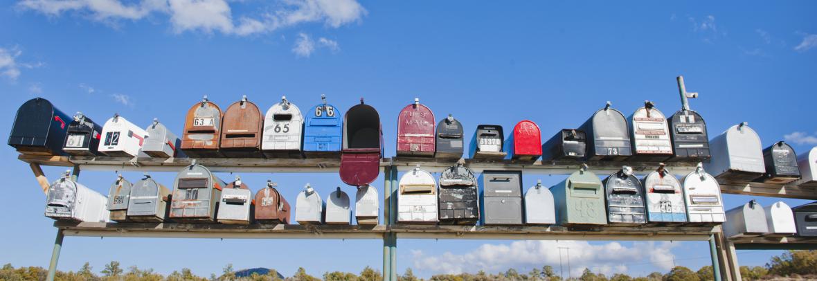 Row of country mailboxes in different colors against a deep blue sky with clouds