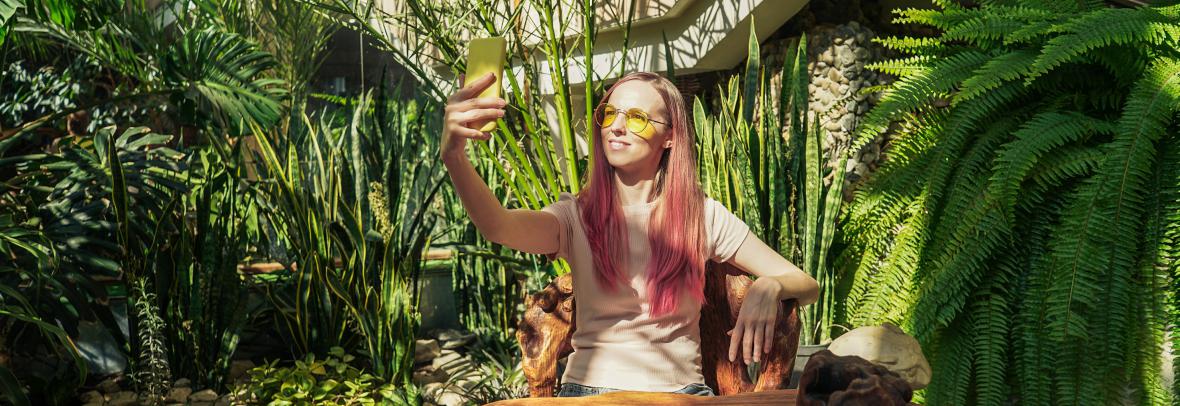 A woman taking a selfie photo amid an inside garden with trees and plants