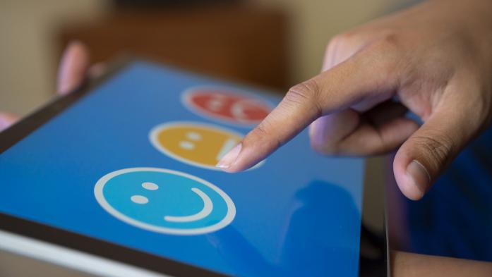 Finger choosing between smiling, neutral and negative faces on an iPad