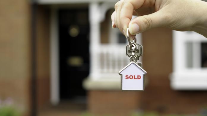 Hand in front of a house holding keychain with "sold" inside small house
