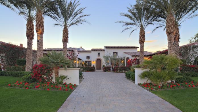 Large luxury home with landscaped entryway bordered by palm trees