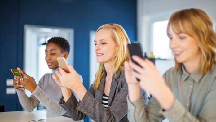 three women in office using cell phones