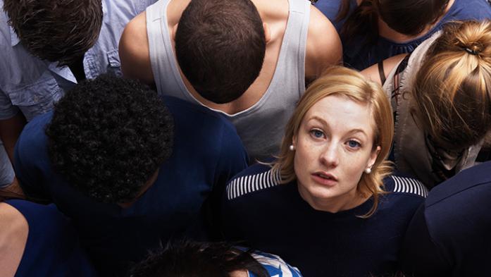 Photo of a woman looking up at the camera among man other people looking down