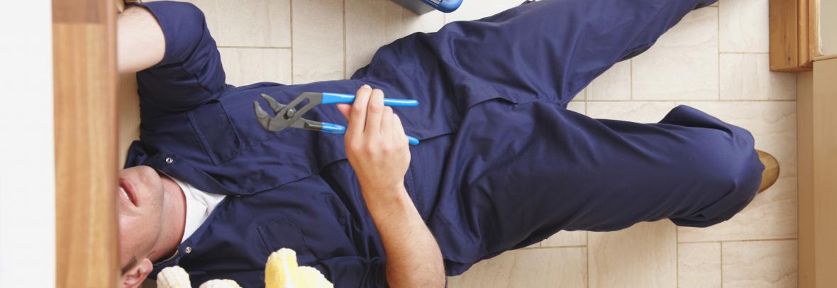 plumber with tools on floor with head under cabinet