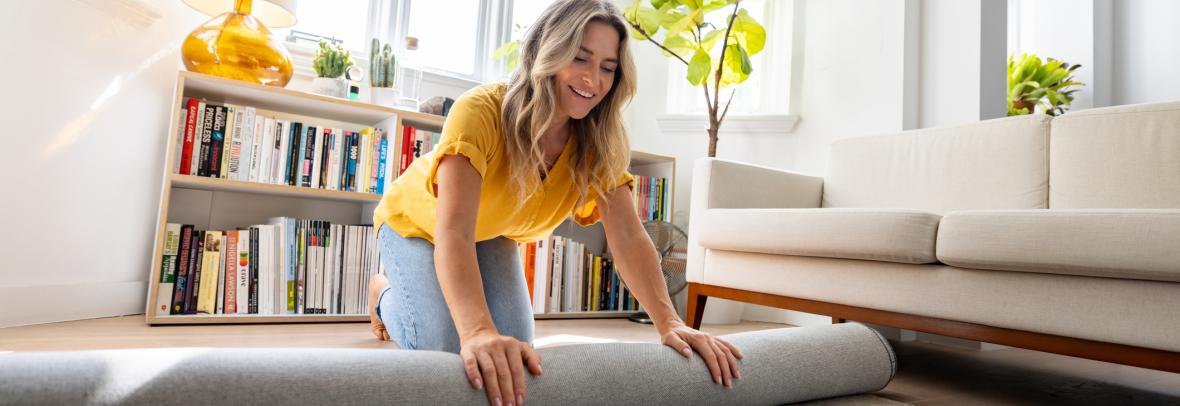 Happy Caucasian woman moving house and unrolling a carpet while unpacking - domestic life concepts