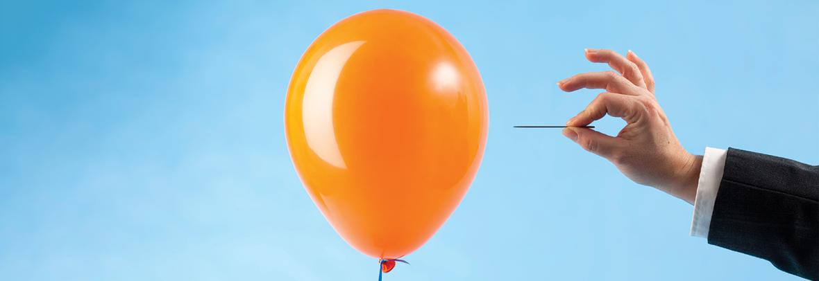 Photo of an orange balloon about to be popped by a person holding a needle
