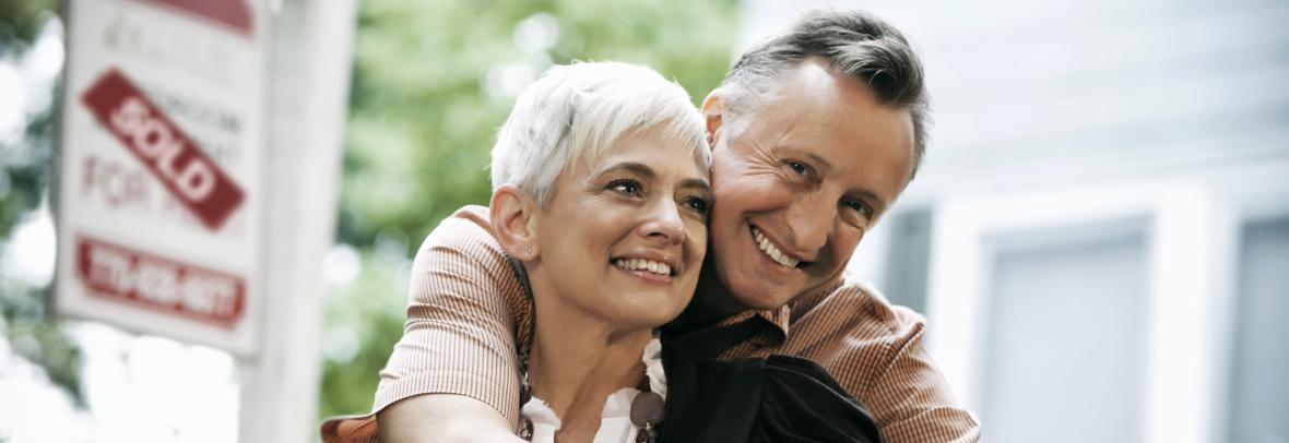 Couple in their sixties in front of a sign that they sold their home