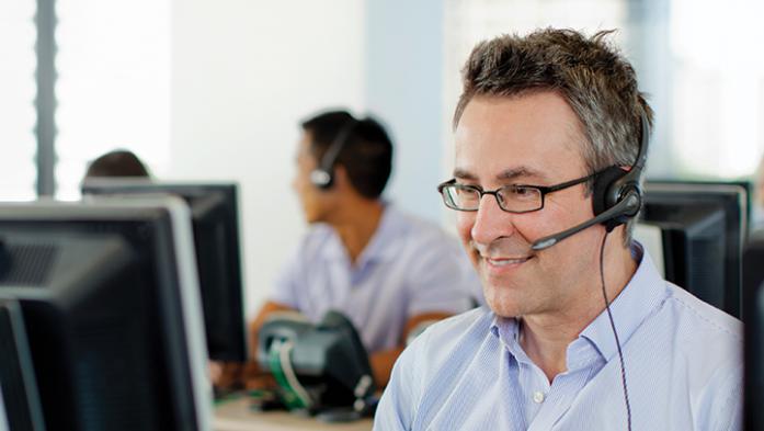 photo of a male tech support person with a headset on in front of a computer
