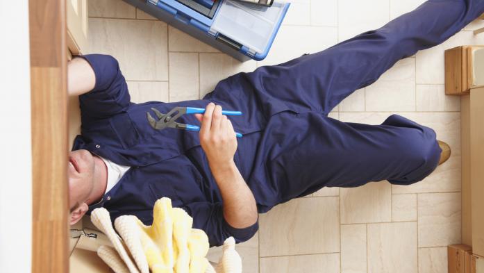 plumber with tools on floor with head under cabinet