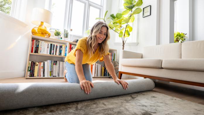 Happy Caucasian woman moving house and unrolling a carpet while unpacking - domestic life concepts