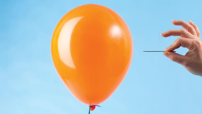 Photo of an orange balloon about to be popped by a person holding a needle