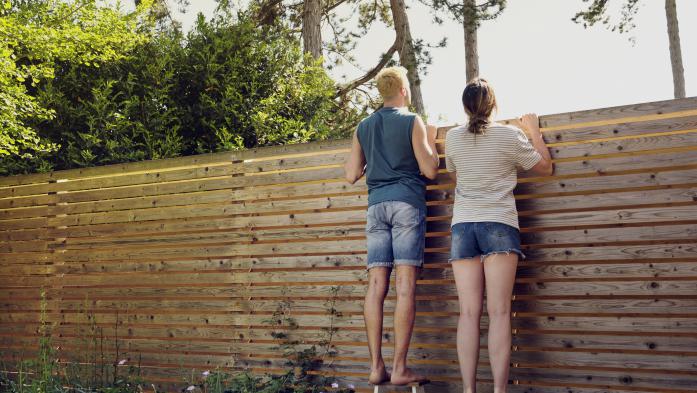 Young couple looking over wooden fence at back yard - stock photo