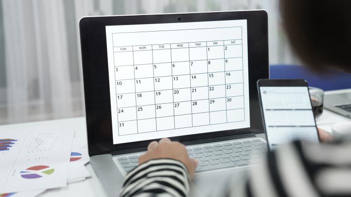 Women work from home using laptop to check time table while reading calendar on mobile phone in hand as well