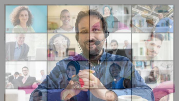 Man at computer overshadowed by other people attending an online class