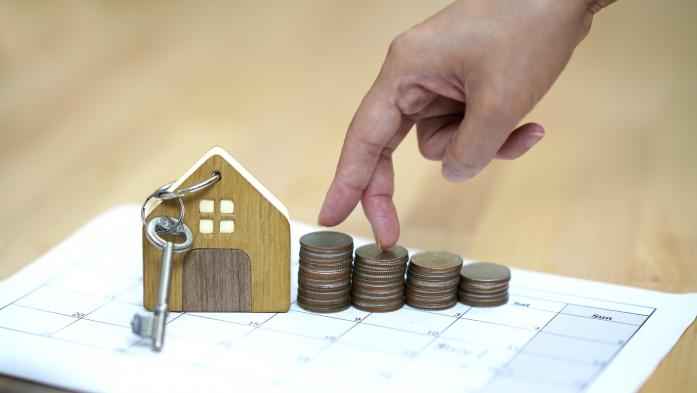 small wooden house with key, hand walking on stacks of coins, all on calendar page